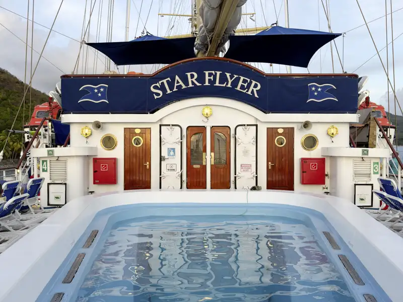 Blick vom Deck über den Pool auf das Heck des Großseglers Star Flyer, der in einem Hafen der Kleinen Antillen ankert.