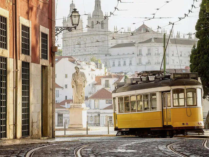 Die berühmte gelbe Straßenbahn Lissabons fährt auf Kopfsteinpflaster durch die Altstadt Alfama mit Blick das Kloster São Vicente de Fora.