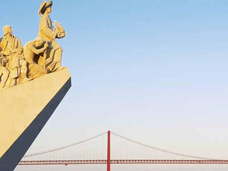 Das Seefahrerdenkmal Padrão dos Descobrimentos in Lissabon mit Blick auf die rote Brücke Ponte 25 de Abril bei blauem Himmel.
