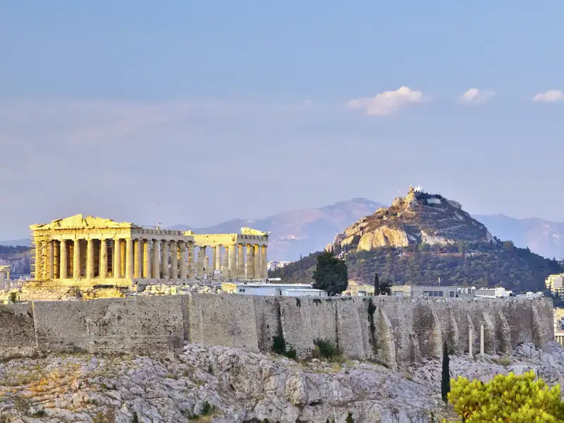 Blick auf den Parthenon-Tempel auf dem Felsen der Akropolis in Athen mit dem markanten Lykabettus-Hügel im Hintergrund.