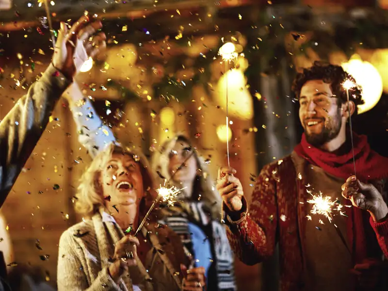 Eine Gruppe feiert mit brennenden Wunderkerzen und Konfetti zu Silvester ins neue Jahr.
