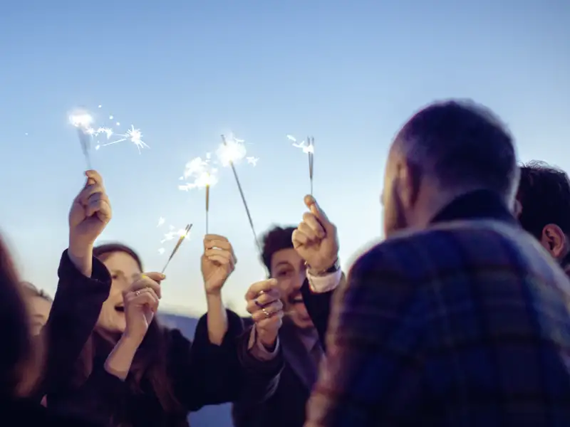 Eine fröhliche Gruppenreise feiert Silvester in Marrakesch und hält Wunderkerzen in den dämmernden Himmel.