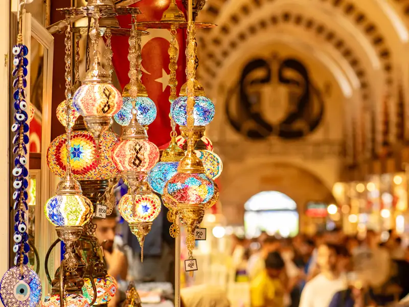 Bunte türkische Mosaiklampen und Nazar-Amulette hängen an einem Stand im belebten Großen Basar von Istanbul.